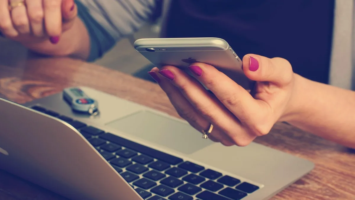 Dizüstü bilgisayarın yanında cep telefonunu kullanan kişi