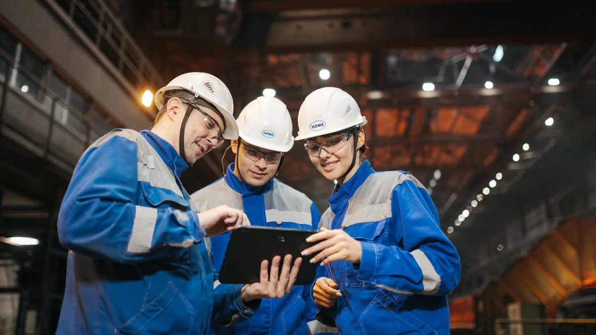 Üretim tesisinde tablet üzerinden birlikte çalışan üç mühendis