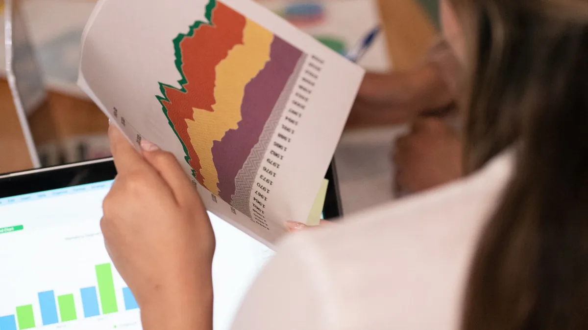 Bilgisayar ekranının önünde basılı grafikleri karşılaştıran kişi