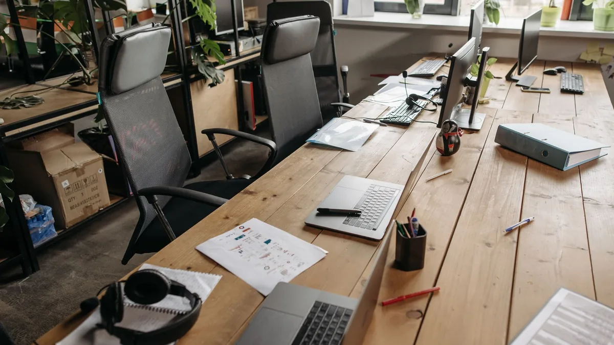 Bilgisayarlar, not kâğıtları ve çalışma araçları bulunan ortak ofis masası