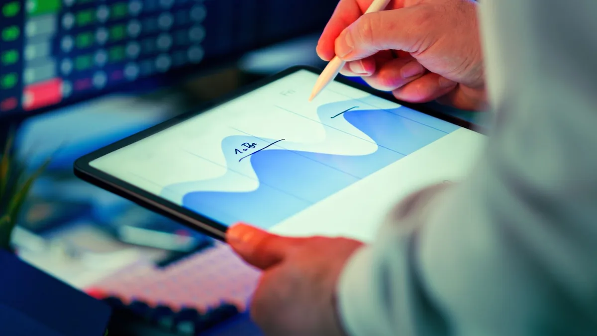 Ofis masasında tablet üzerindeki veri grafiğini kalemle inceleyen kişi
