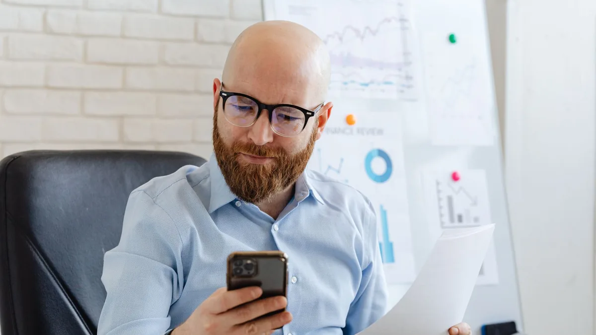 Telefon ve basılı raporu birlikte inceleyen ofis çalışanı
