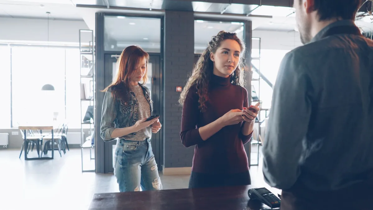 Kafe tezgahında telefon kullanan müşteriler ve çalışan