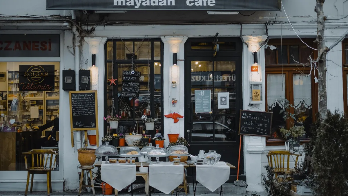 Sokakta masa ve menü panoları bulunan küçük bir kafe cephesi