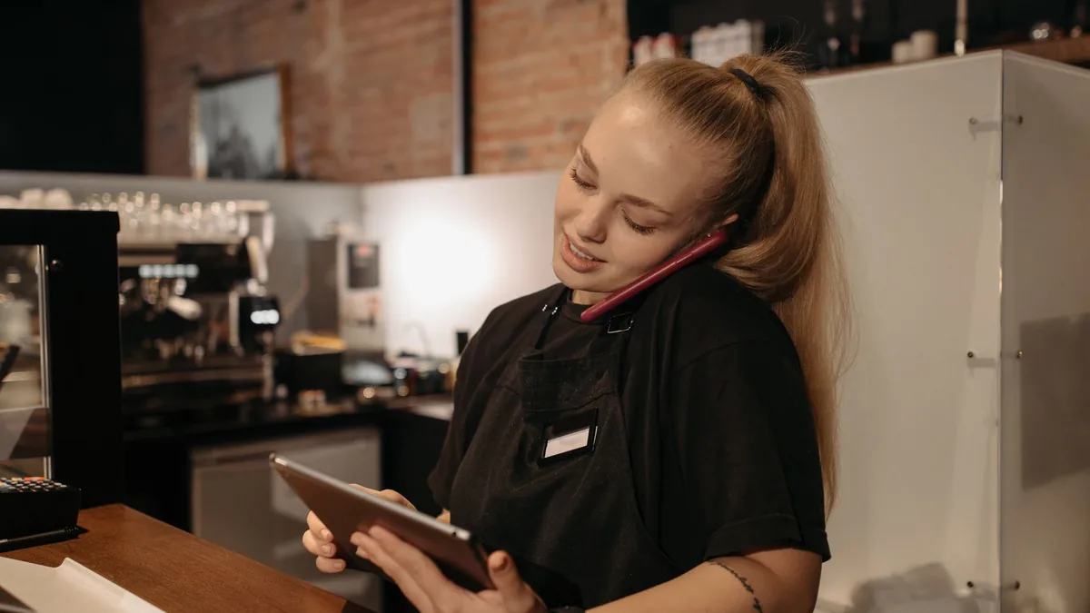 Kafe tezgâhında telefon ve tabletle sipariş yöneten görevli