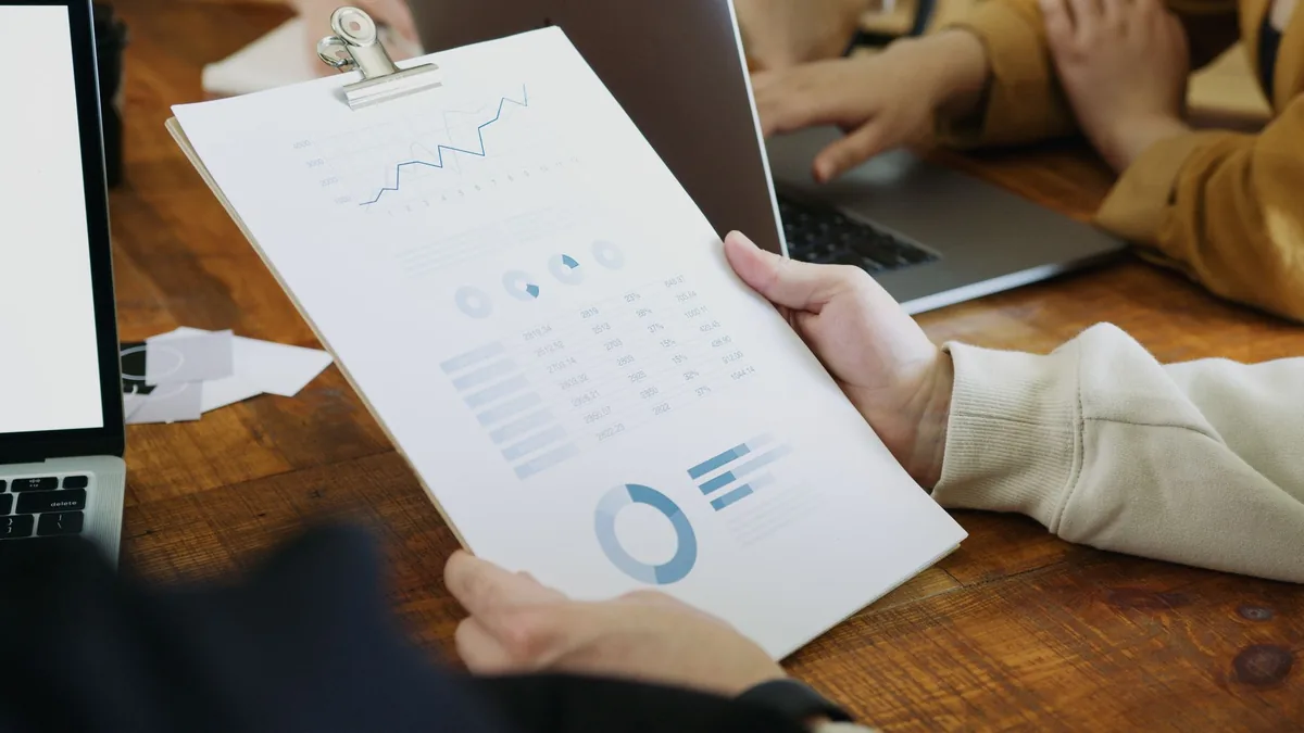 Grafik bulunan belgeyi tutan kişinin elleri ve dizüstü bilgisayar