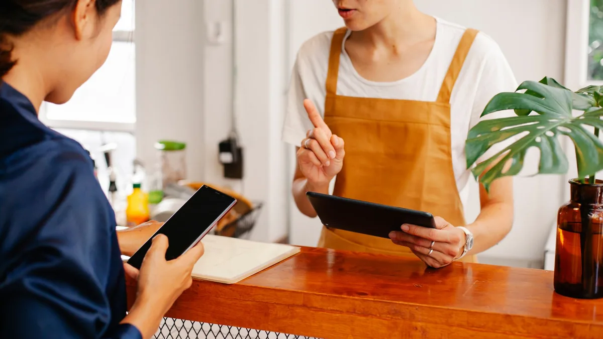 Kafe tezgâhında telefon ve tablet kullanan iki çalışan