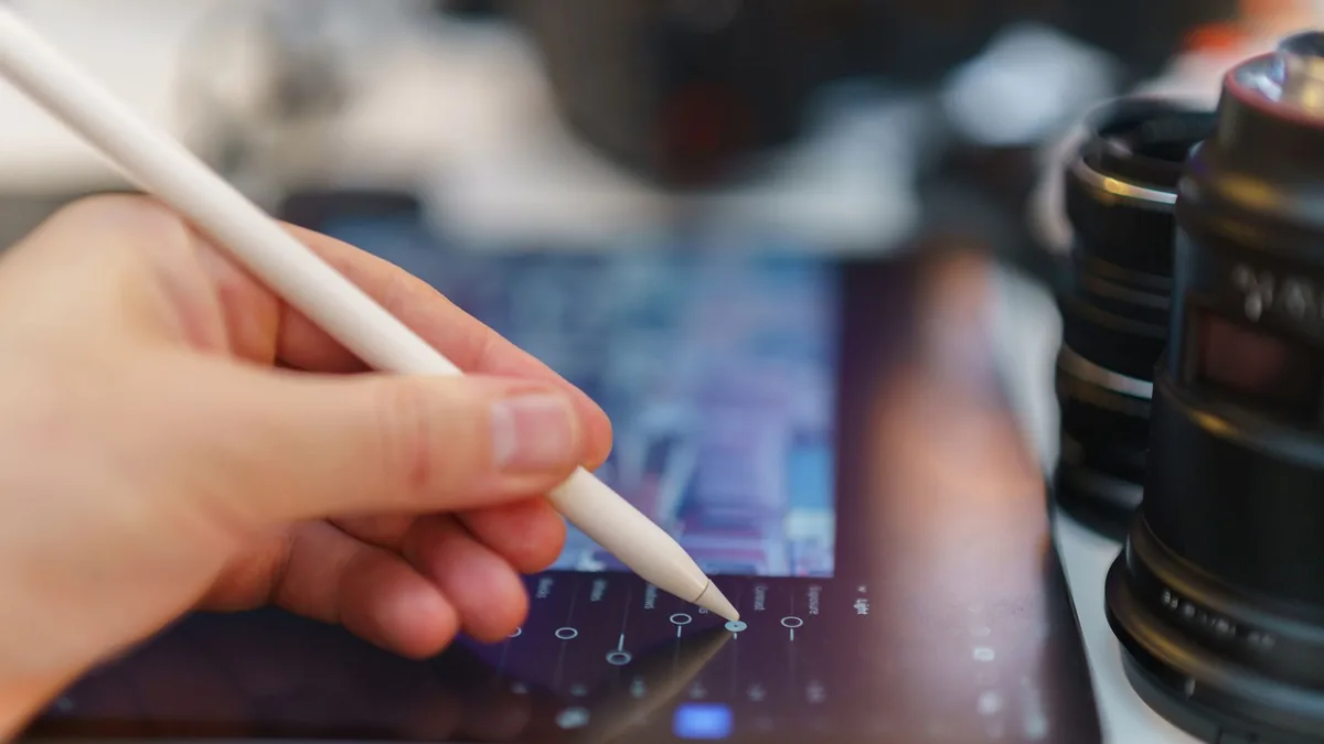 Kalemli tablet üzerinde görsel düzenleyen kişinin eli ve kamera objektifi