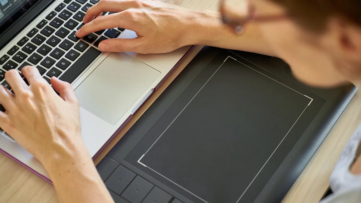 Dizüstü bilgisayarın yanında kalemli tablet kullanan kişi