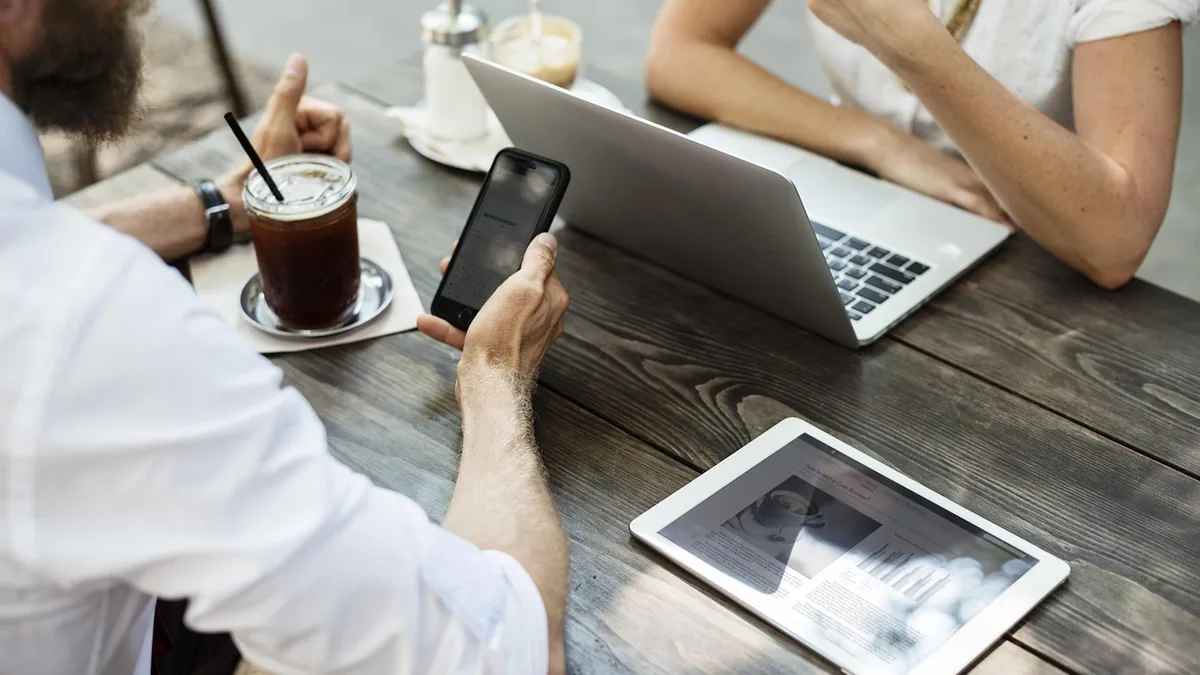 Telefon, tablet ve dizüstü bilgisayar bulunan masada görüşen ekip
