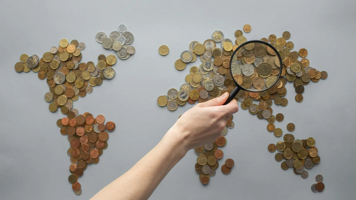 Madeni paralardan oluşturulmuş dünya haritasını büyüteçle inceleyen el