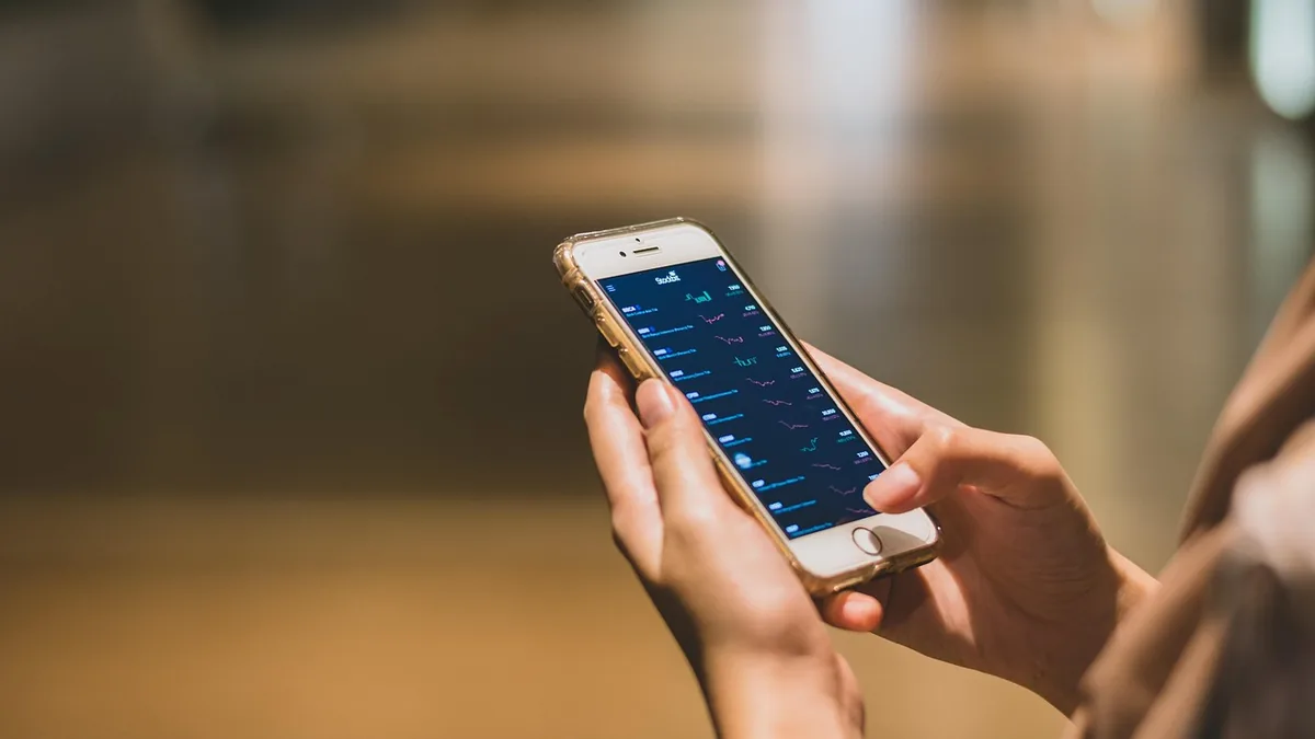 Ekranında finans grafiği bulunan cep telefonunu tutan eller