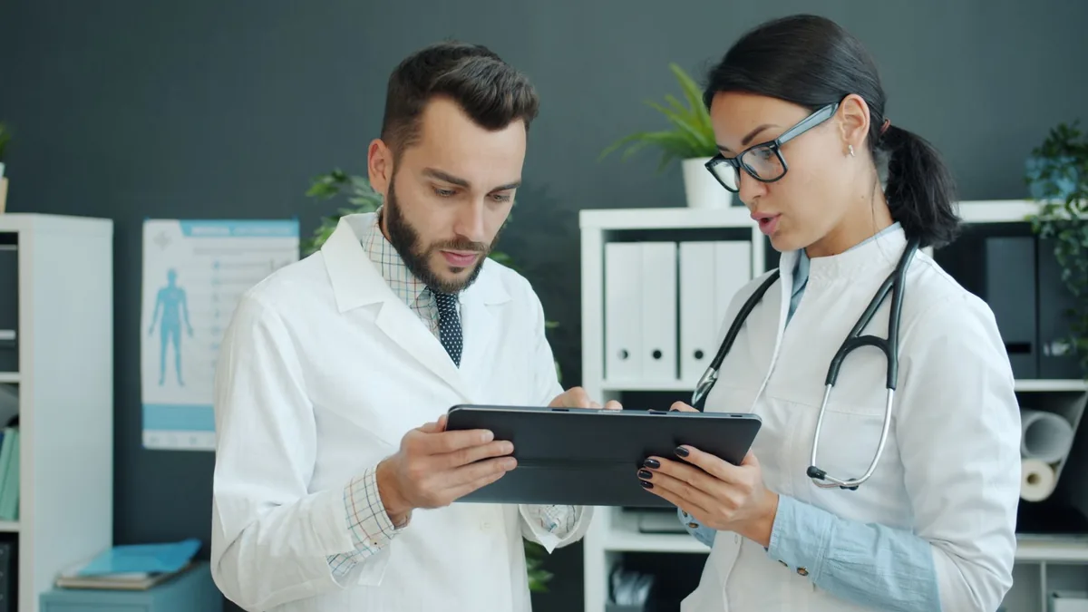 Klinik ortamında tablet ekranındaki bilgileri görüşen iki hekim