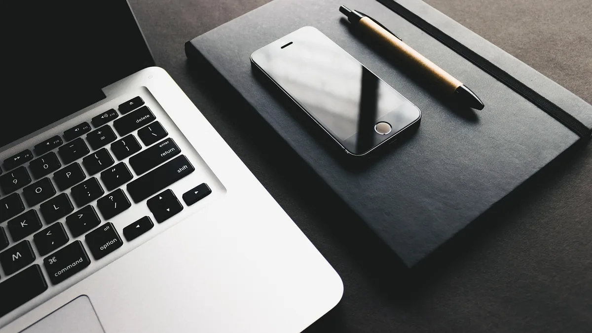 Dizüstü bilgisayar yanında siyah defter, kalem ve telefon